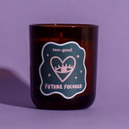 Brown glass candle vessel with 'two-good' and 'Future Focused' label on a purple background. Linear illustration. Woody, spicy scent