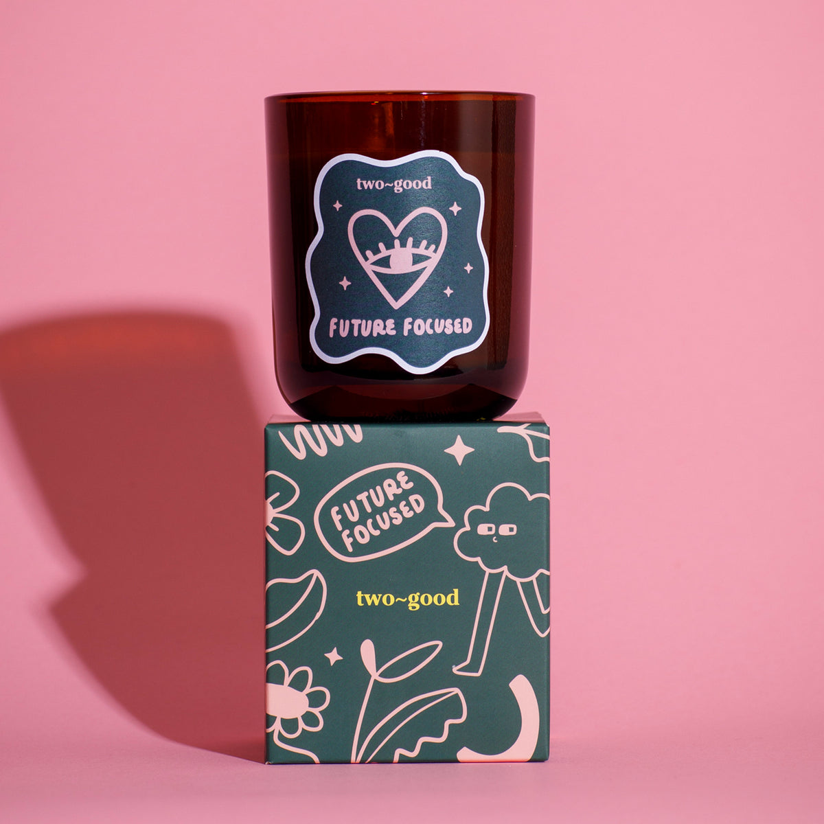 Candle with 'two-good' branding on a 
pink background. Illustration on box. Linear. Branded candle box