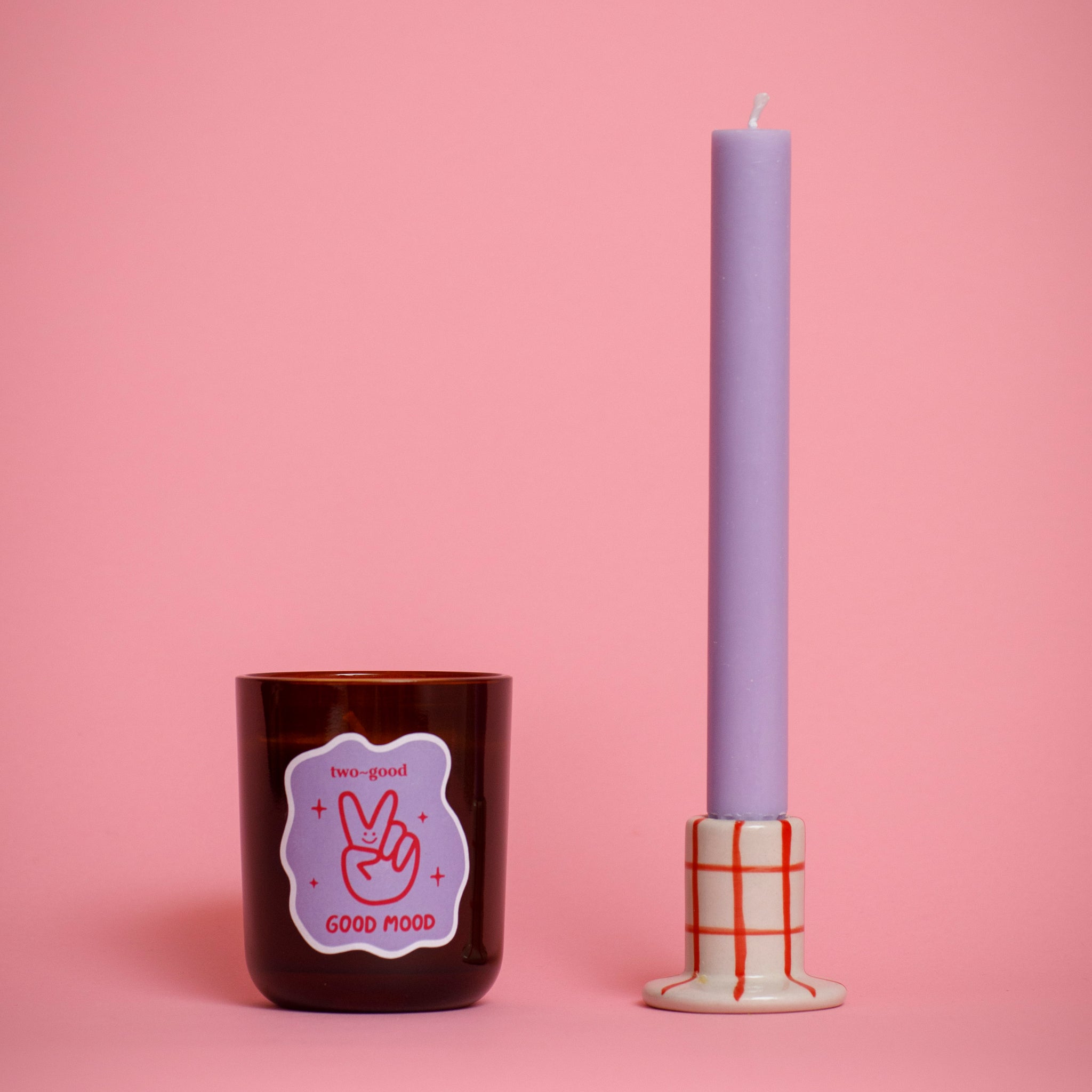 Brown glass candle vessel with a sticker and a tall purple candle on a pink background grid candlestick holder fruity scent soy wax candle 