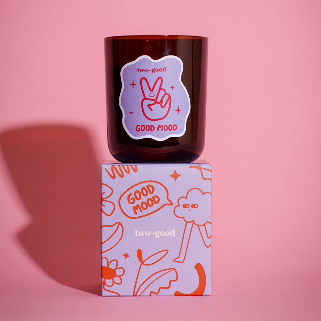 Candle with 'Good Mood' label on a matching box against a pink background bold linear illustrations fruity scent