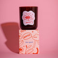 Brown glass candle vessel with 'two-good' branding on a pink background illustrations on packaging fun soy wax candle