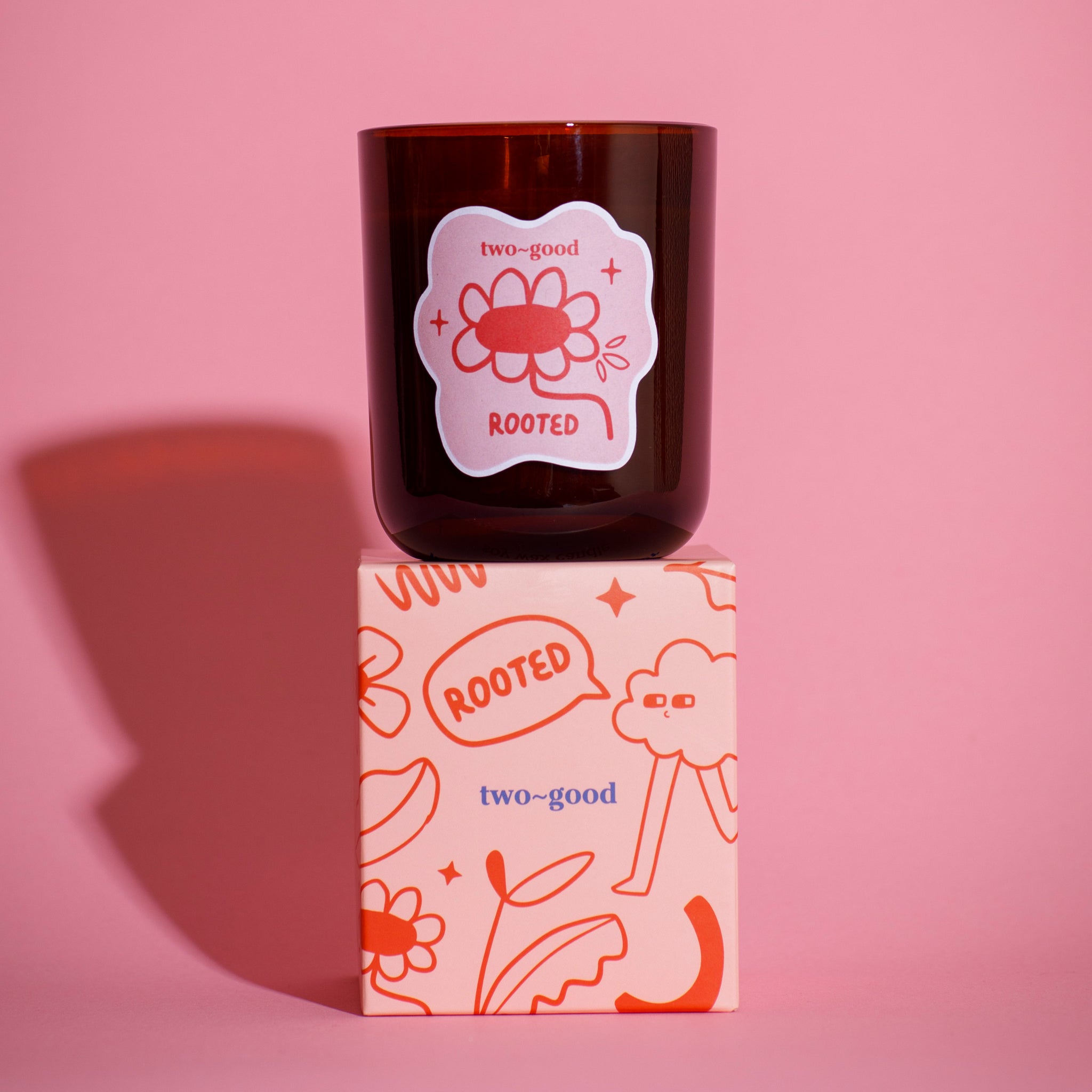 Brown glass candle vessel with 'two-good' branding on a pink background illustrations on packaging fun soy wax candle