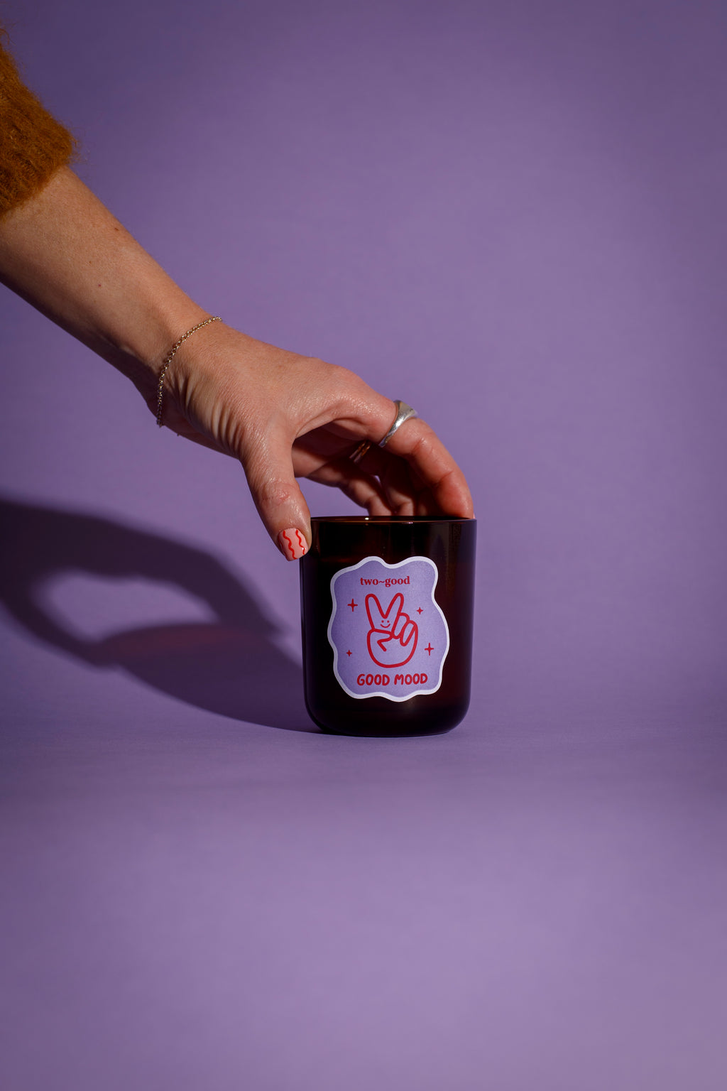 Hand holding a brown glass candle vessel with a peace sign design against a purple background soy wax candle 