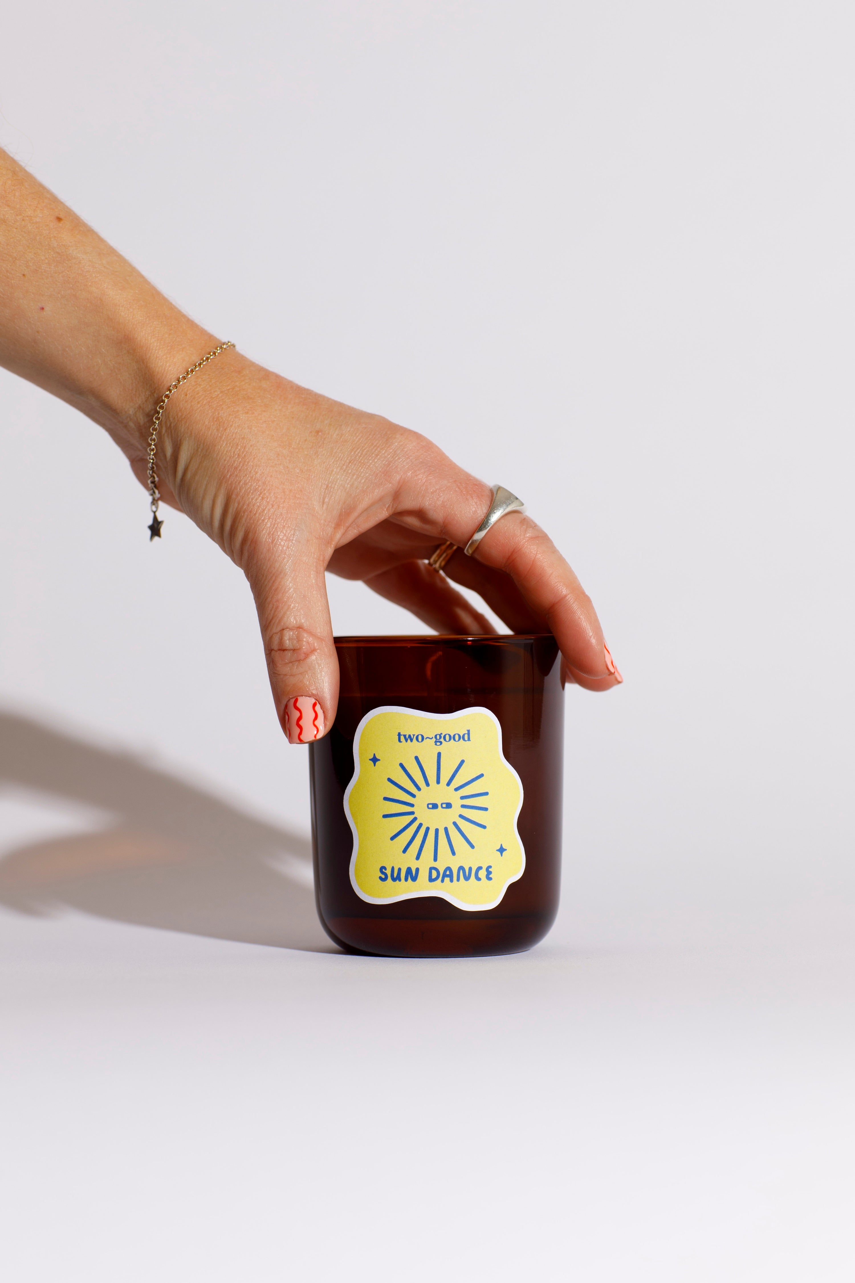 Brown candle vessel with illustration on sticker. Hand holding the candle 