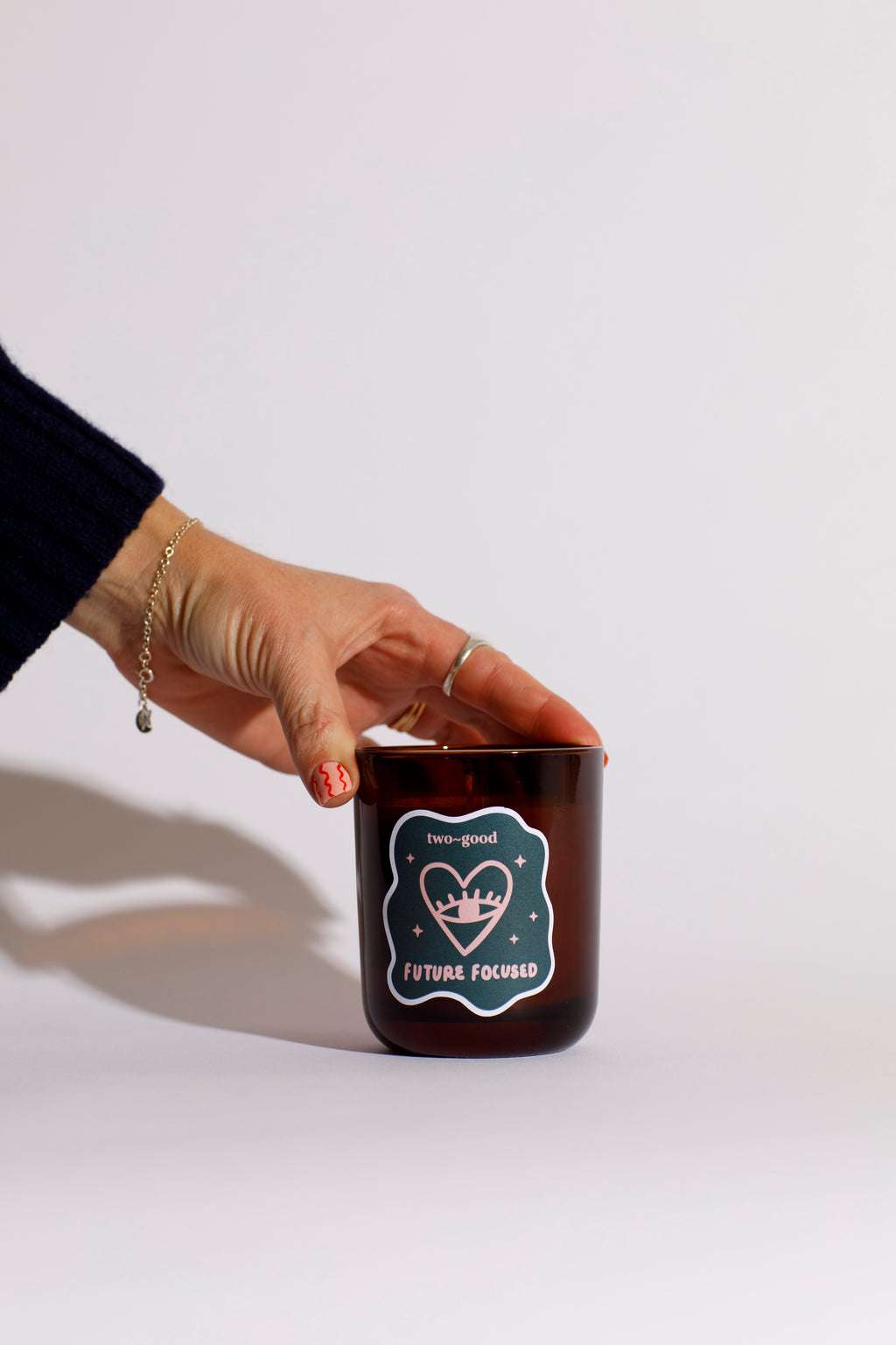 Hand holding a brown glass candle vessel with a label on a white background. Heart linear illustration