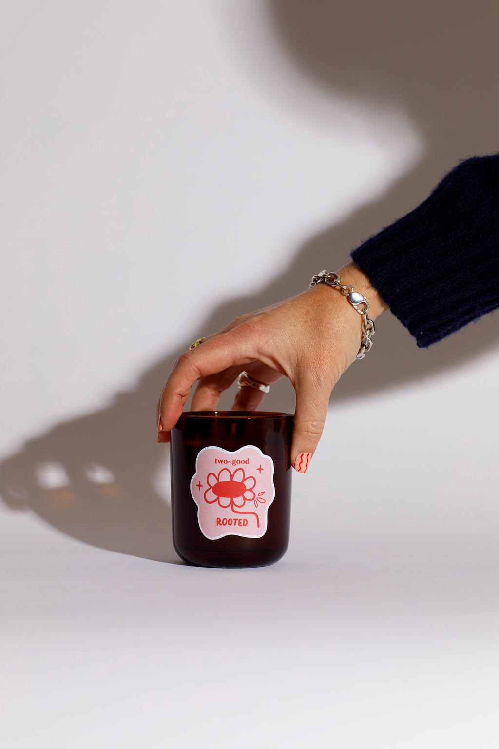 Hand holding a brown glass candle vessel with a pink label against a white background bold floral design on candle