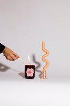Person lighting a candle with a match, next to a spiral-shaped candle on a plain background soy wax candle