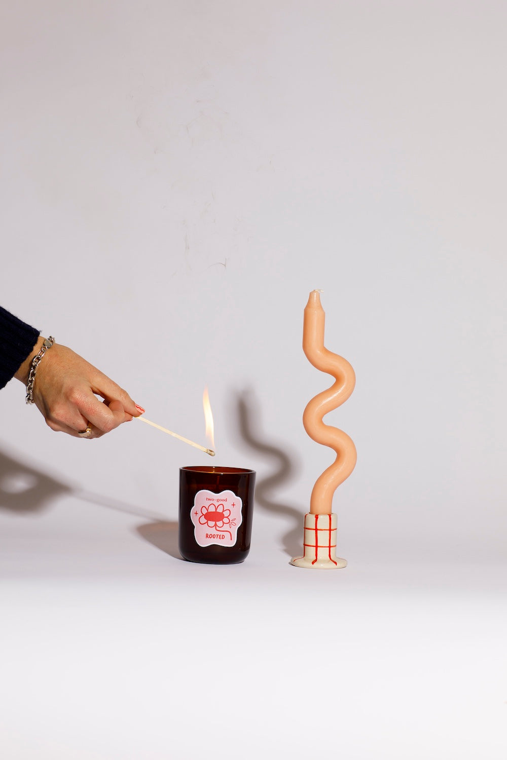 Person lighting a candle with a match, next to a spiral-shaped candle on a plain background soy wax candle