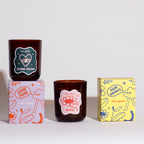 Two brown glass candle vessels with linear illustrations on labels and two boxes featuring branding on a light grey background