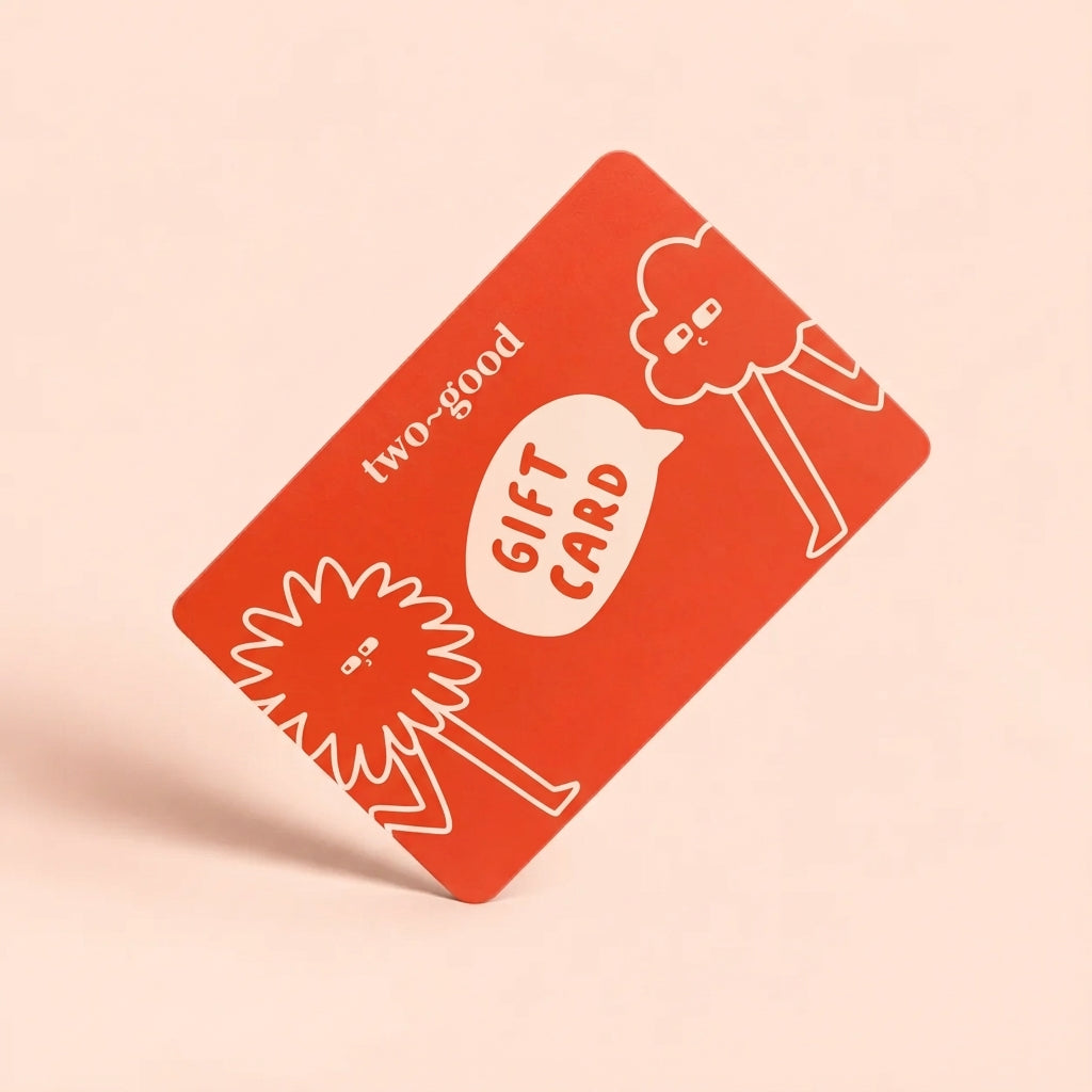 A red gift card with white line art illustrations and the text 'two-good' and 'GIFT CARD', shown floating at an angle on a light peach background.