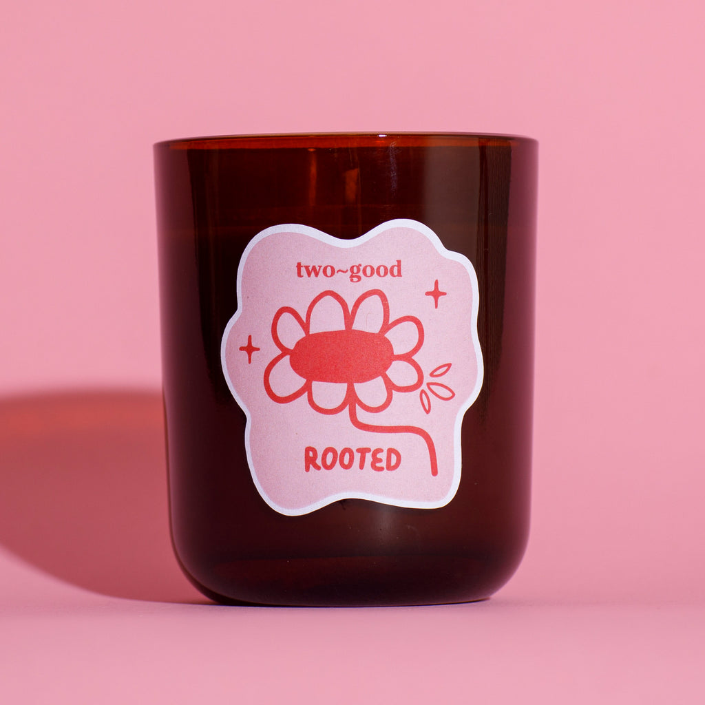 Brown glass candle vessel with a pink label featuring a flower design on a pink background soy wax candle